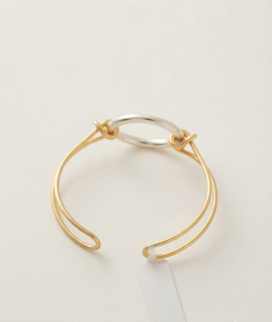Gold and silver two-tone open kada bracelet with interlocking twisted knot design on a cream background