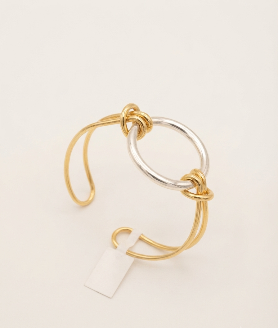 Gold and silver two-tone open kada bracelet with interlocking twisted knot design on a cream background