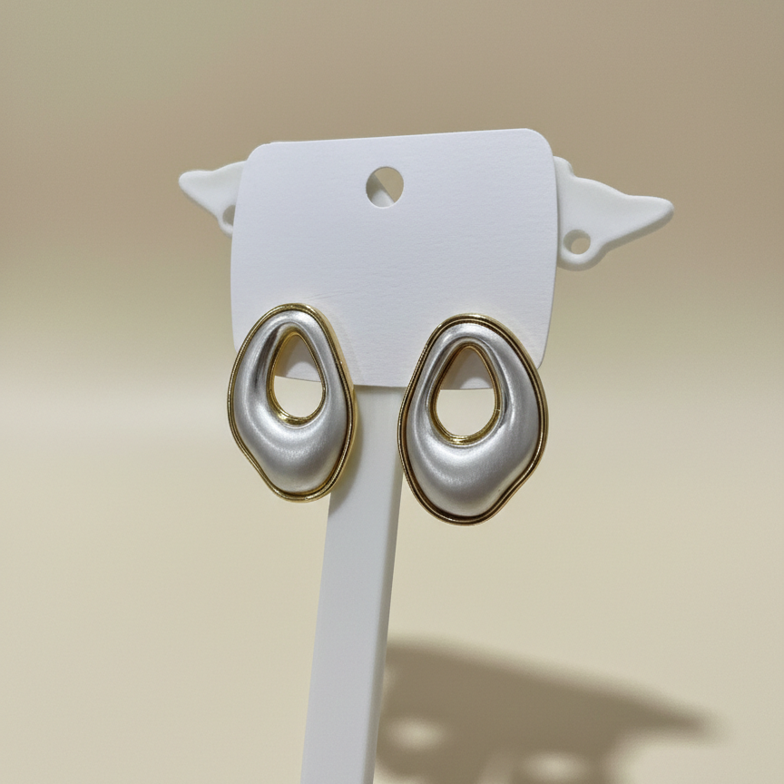 Pair of gold and white earrings on a white stand with a beige background