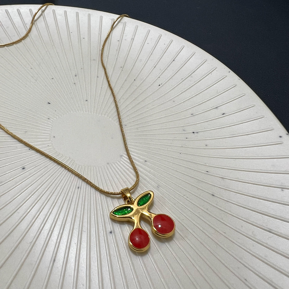 Front view of a gold plated stainless steel cherry necklace hanging on a professional wooden jewelry stand