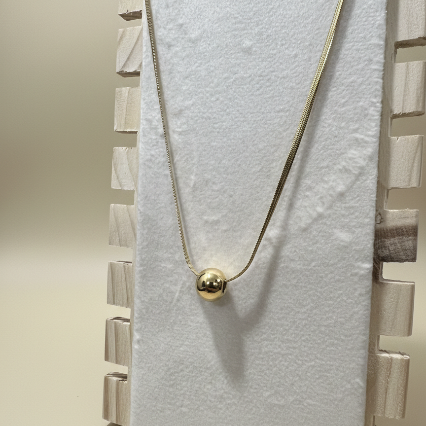 minimalist gold plated spherical bead pendant on a sleek snake chain necklace displayed on a wooden jewelry stand