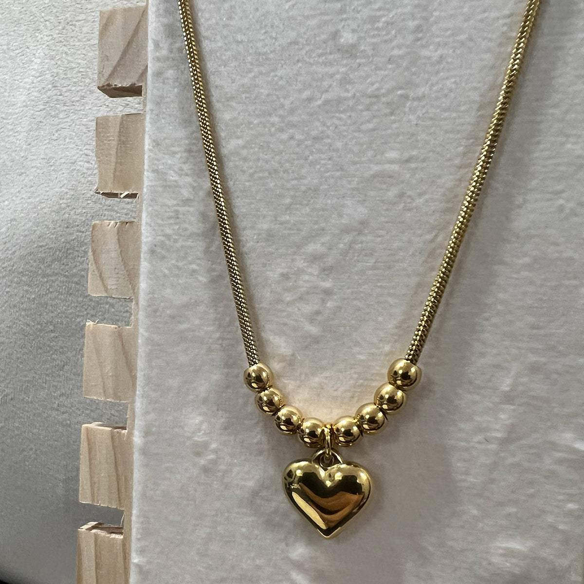 Flat lay view of a gold plated heart pendant necklace featuring spherical beads on a white textured decorative plate