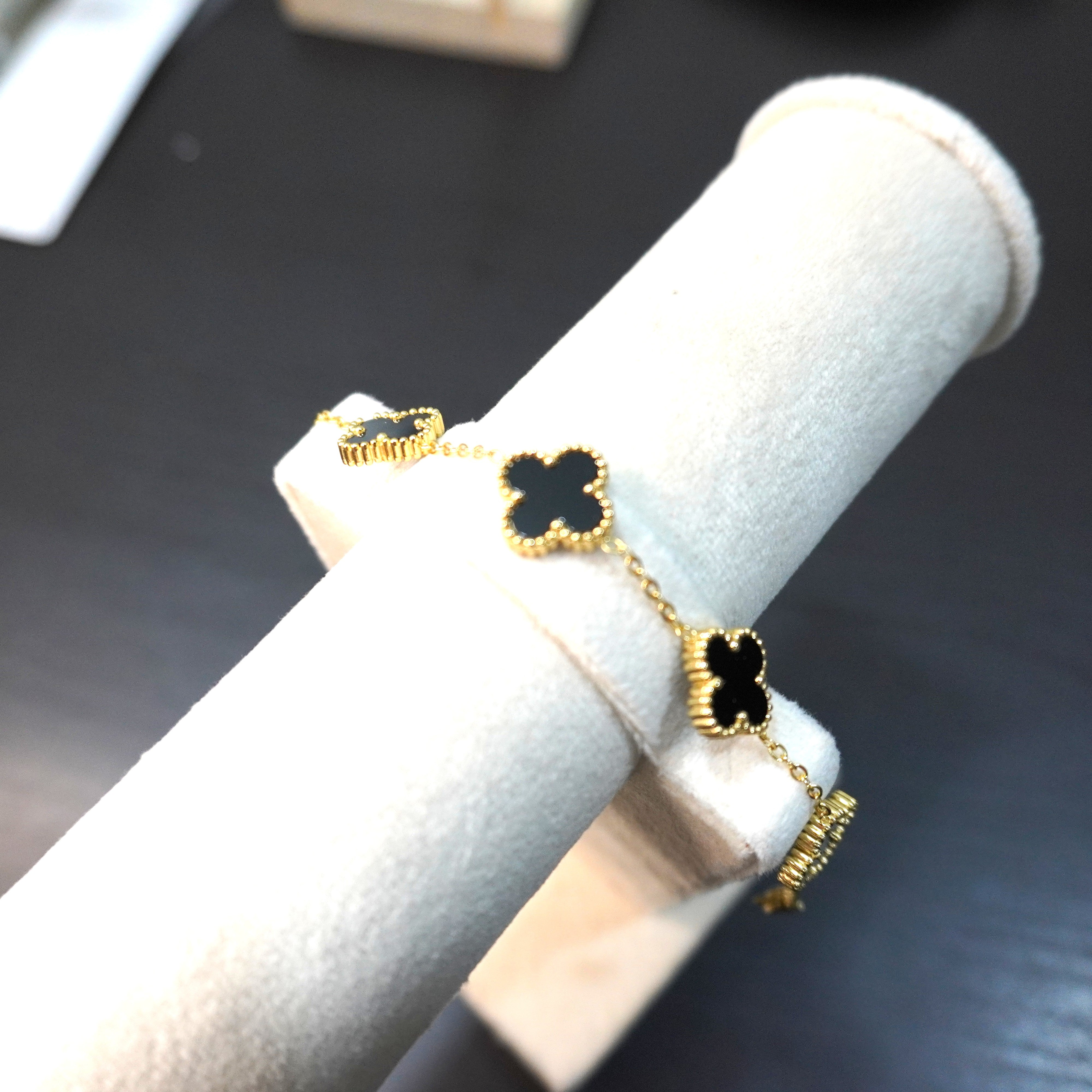 Gold and black clover-shaped earrings on a white cushioned stand.
