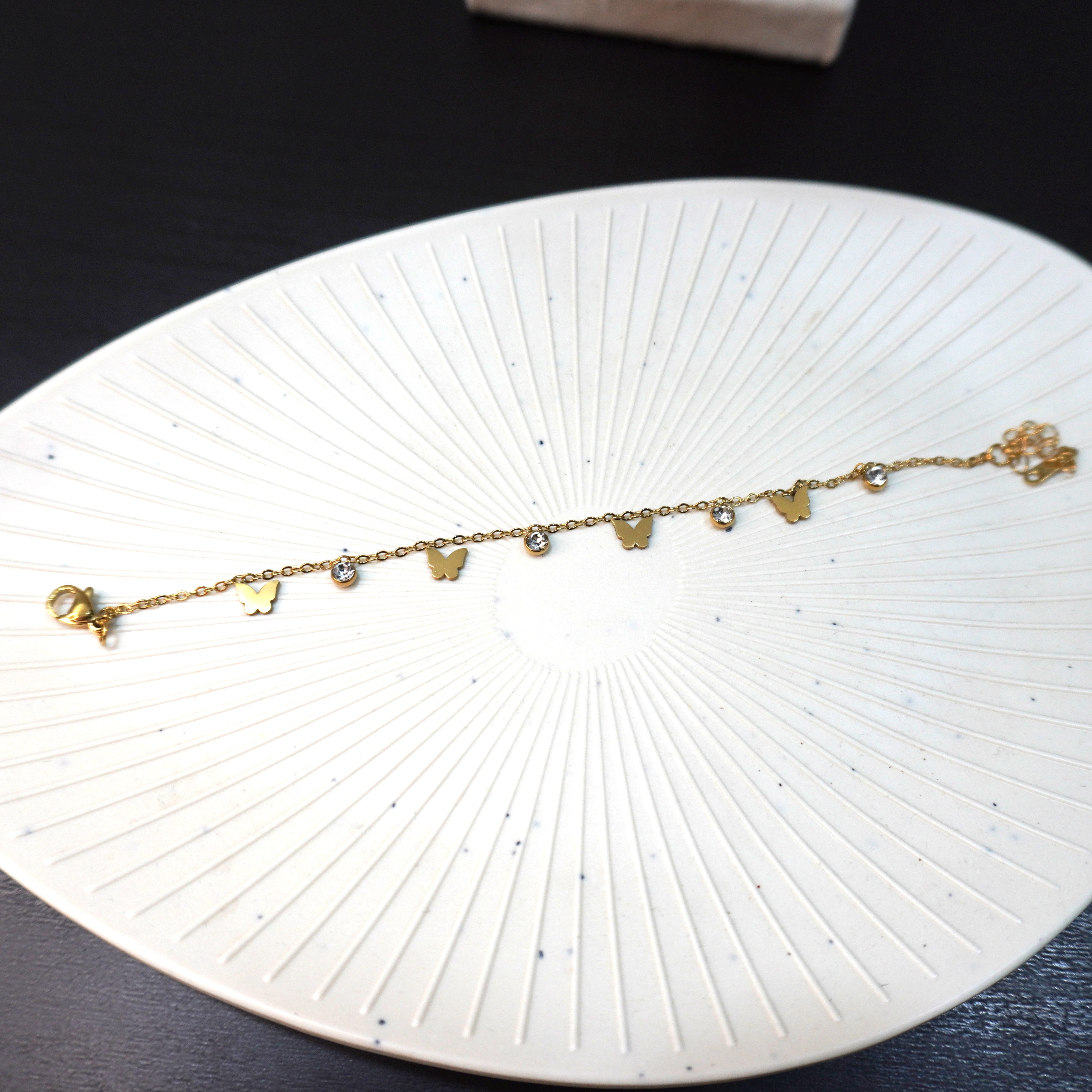 Gold bracelet with butterfly charms on a white circular dish