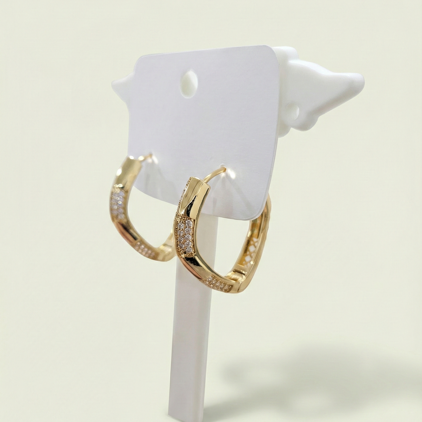 Close up of geometric gold plated hoop earrings with pave stone detailing on a white jewelry display stand