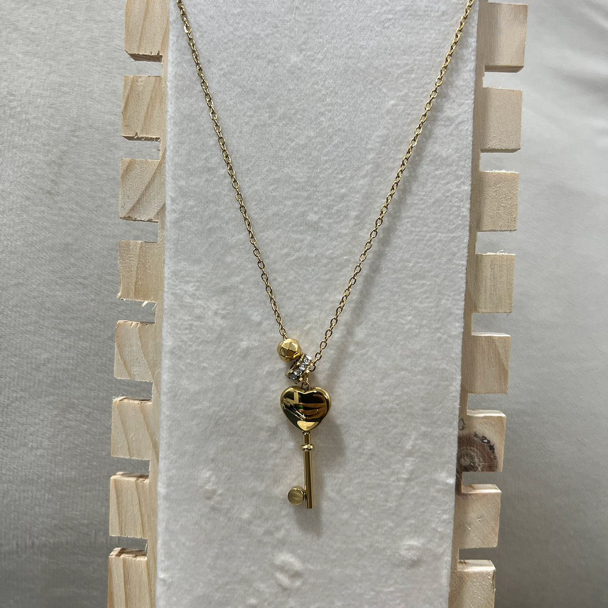 Polished gold heart key necklace for women displayed vertically on a professional wooden jewelry stand