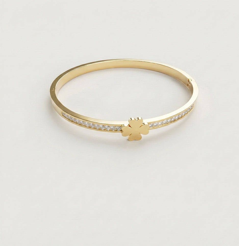 Top view of a gold plated clover bangle with crystal embellishments on a neutral background