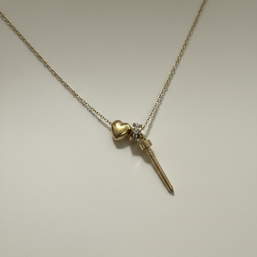 Gold plated stainless steel necklace featuring heart and spike charms with crystal accents on a white textured background