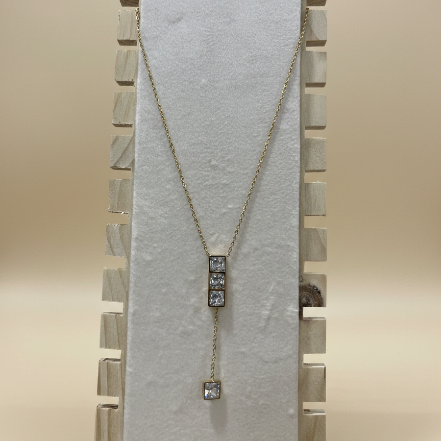 Side profile of a premium anti-tarnish gold finish necklace with a geometric crystal drop on a display stand