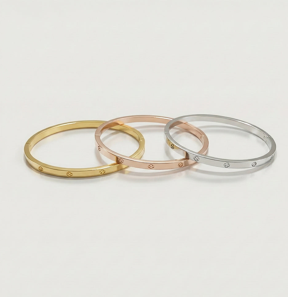 A set of three clover-etched bangles in gold, rose gold, and silver finishes displayed on a clean white surface