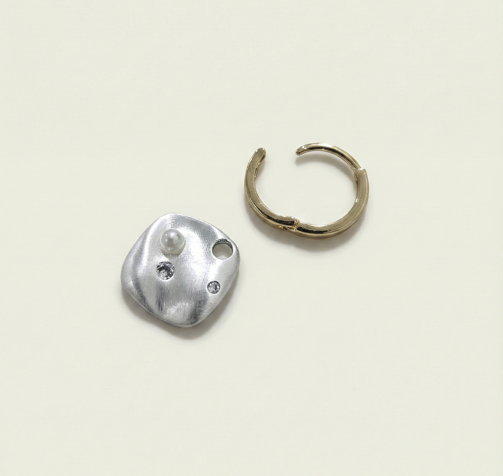 Pair of two-tone gold and silver earrings with organic pearl charms displayed on a premium white jewelry stand.