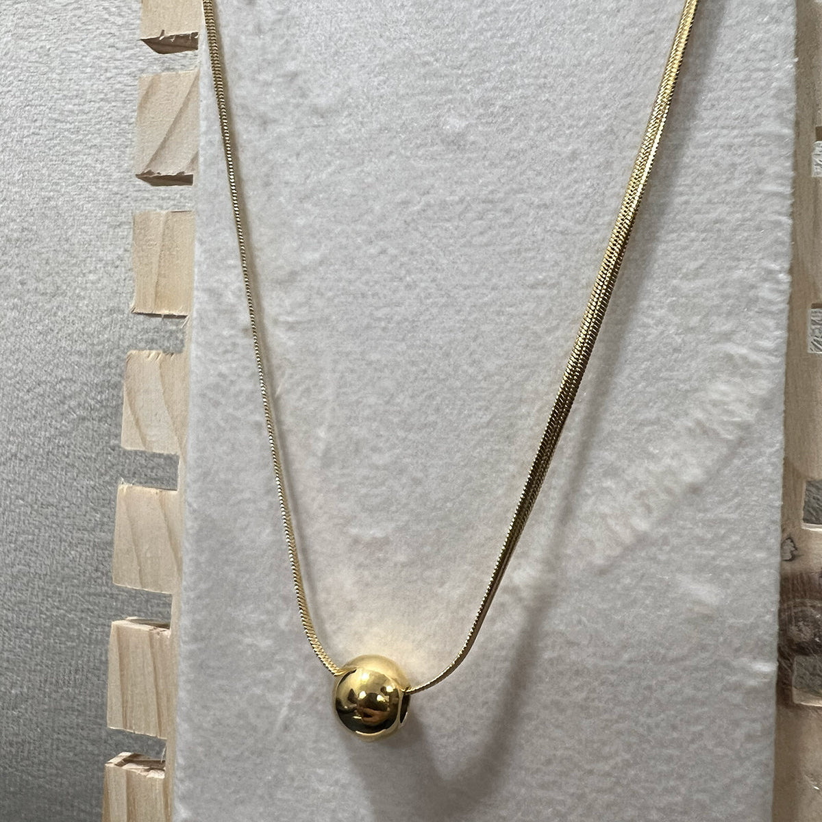 Close-up of a high-shine gold toned ball necklace in stainless steel highlighting the polished spherical charm.