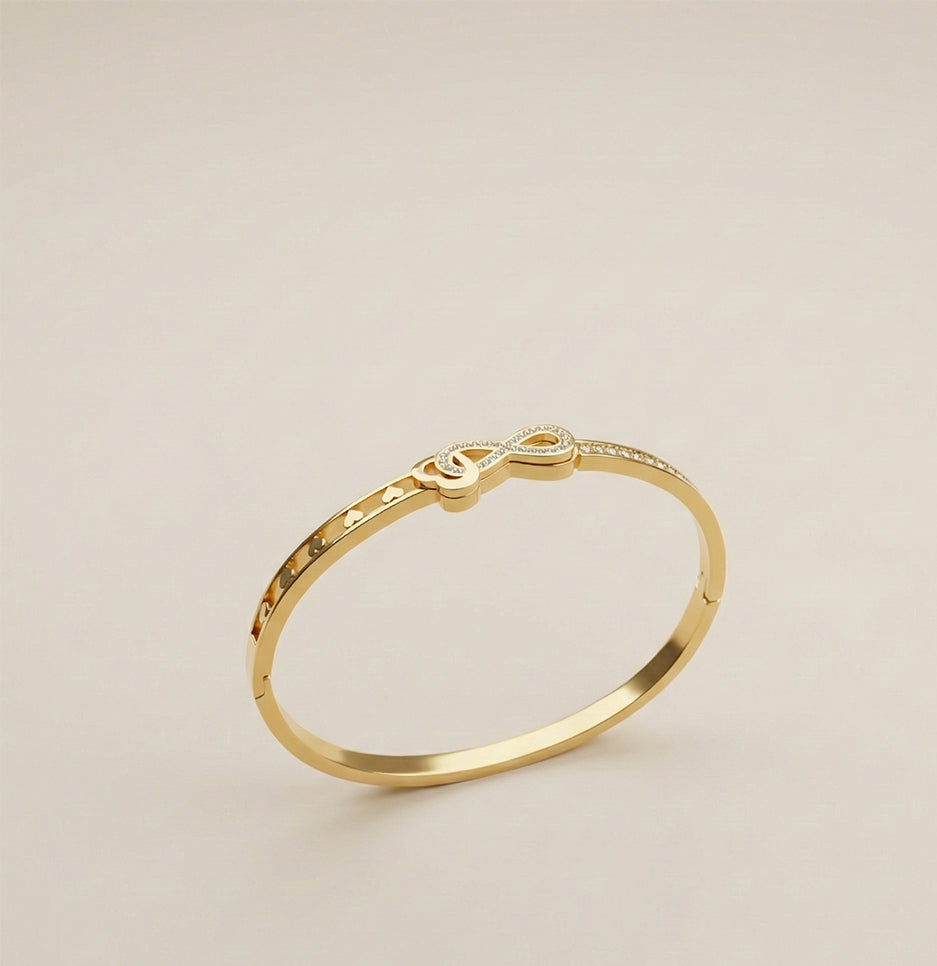 Gold plated infinity bracelet with heart cut-outs and crystal accents displayed on a neutral background