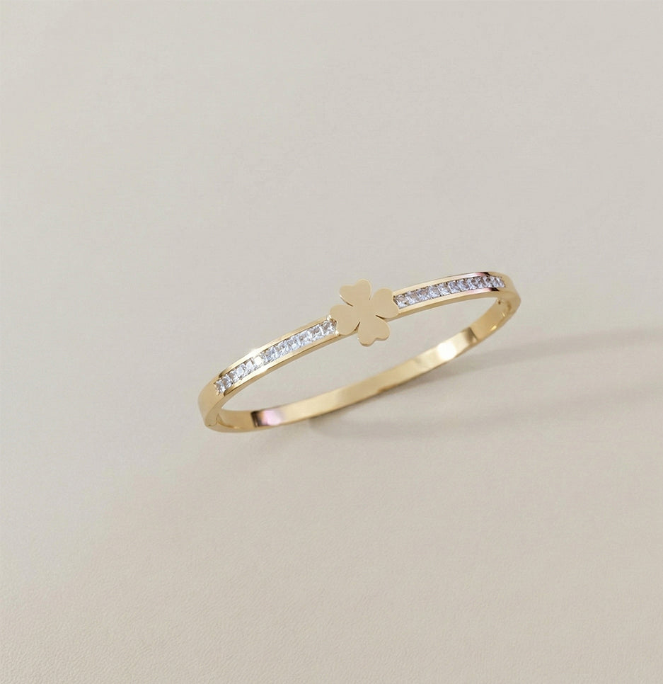 Angled view of a minimalist gold plated bangle featuring a central clover charm and shimmering crystals
