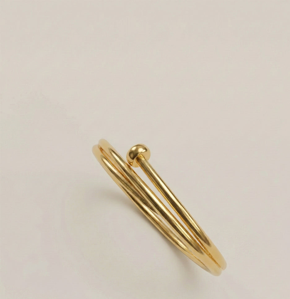 Angled studio shot of a modern gold-plated stainless steel nail bangle against a neutral background
