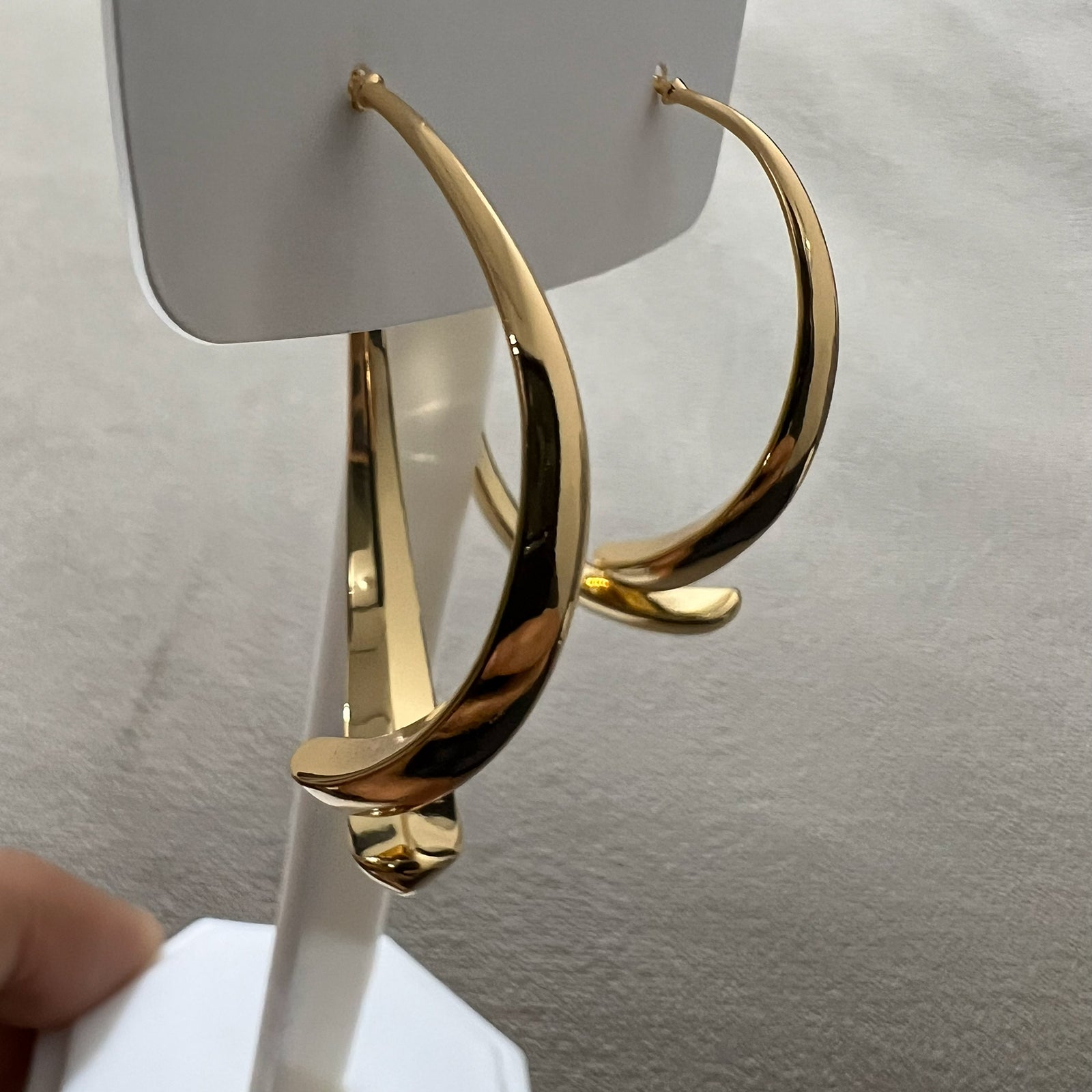 High-shine modern tapered hoop earrings in gold-toned stainless steel displayed on a minimalist white pedestal