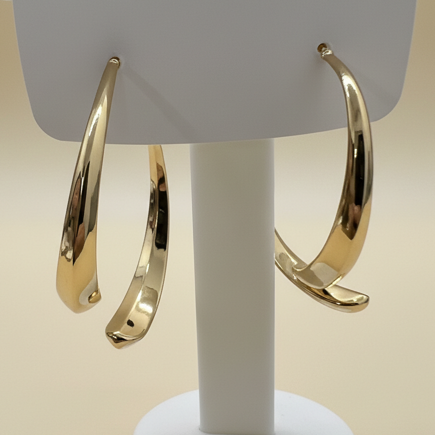 A close-up angled shot of bold, tapered gold-plated hoop earrings on a white jewelry stand - zwelzy design