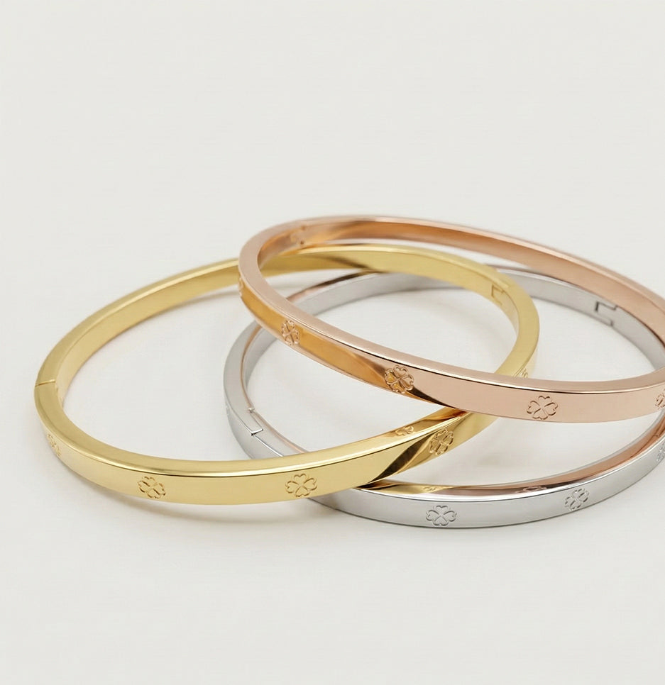 Angled view of three stackable anti-tarnish clover motif bracelets made from premium gold-plated stainless steel