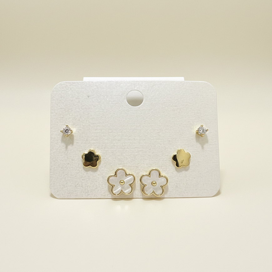 A set of three gold plated stud earrings featuring floral designs and crystals on a white display card.