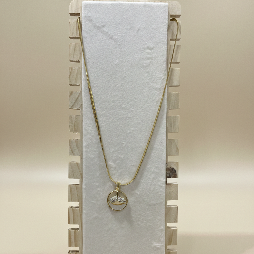 Close-up of a circular mermaid tail pendant in a gold finish displayed on a white textured stand.